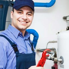 Ein Handwerker lächelt, während er einen roten Schraubenschlüssel in einer modernen Heizungsanlage hält.