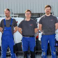 Fünf Männer in blauen Overalls stehen lächelnd vor einem Lieferwagen, bereit für ihre Arbeit im Freien.