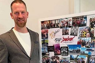 Ein Mann präsentiert eine Collage voller Erinnerungen Ein Mann in einem grauen Blazer steht stolz vor einer Collage mit Fotos von Team-Events und besonderen Momenten.